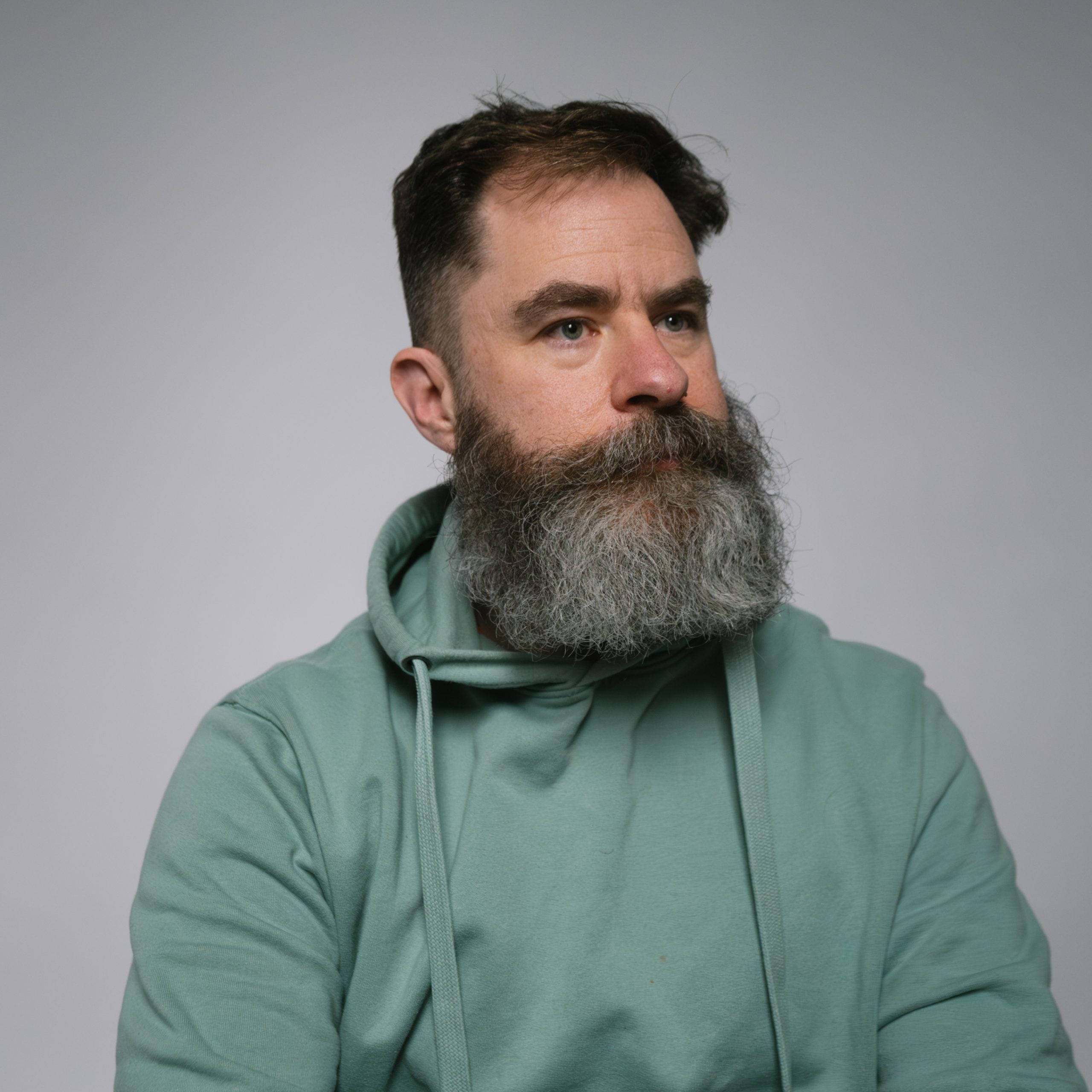 Will is a middle aged white man with a greying beard. He is wearing a green hoodie.